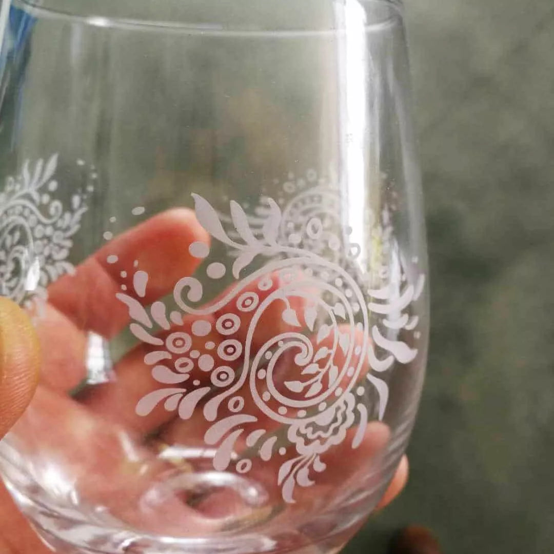 Clear glass with white floral pattern engraved with UV laser held by a hand against a blurred background